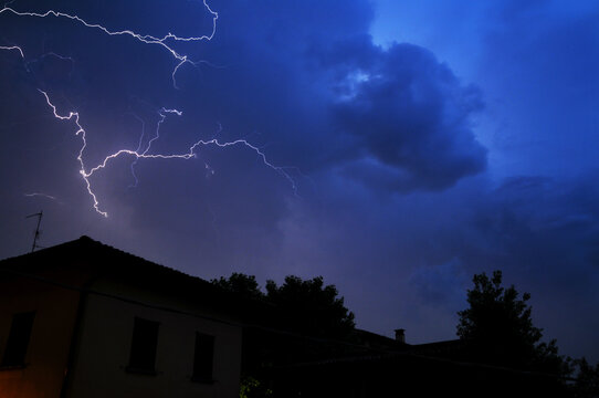 Powerful thunderstorm with lightning in night sky illuminate the clouds with purple-blue hues