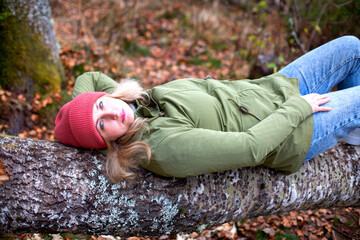 middle-aged caucasian man in hat and jacket is lying on the log in the autumn forest