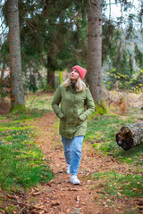 middle-aged caucasian woman in hat and jacket is walking by trail in the autumn forest 