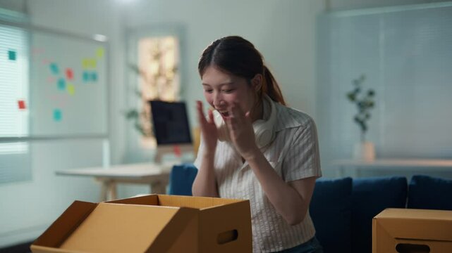 Young woman is unpacking a cardboard box in her home office and is really happy with what she found inside