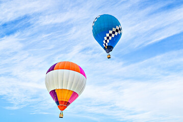 Colorful hot air balloon flying over blue sky with white clouds