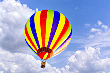 Colorful hot air balloon flying over blue sky with white clouds