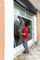 A window cleaner using a squeegee to clean the glass storefront of a retail shop