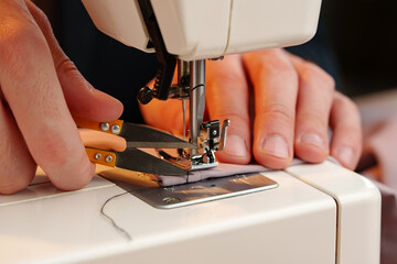Hands sewing fabric using a sewing machine on a wooden table in a well-lit workspace