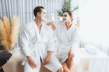 Blissful couple in bathrobe with facial cream mask enjoying serene ambiance of spa salon resort or hotel during holiday. Pampering face spa and skincare treatment with essence relaxation. Quiescent