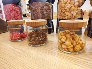 Sweet fried multicolored airy popcorn in glass jars on the shop window