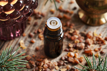 A bottle of myrrh essential oil with a candle and spruce branches