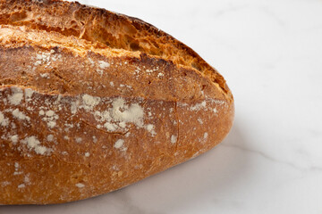 This image showcases a freshly baked, crispy golden bread loaf on a pristine marble kitchen surface, highlighting the texture and artisanal quality of the bread.