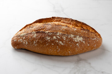 This image showcases a freshly baked, crispy golden bread loaf on a pristine marble kitchen surface, highlighting the texture and artisanal quality of the bread.