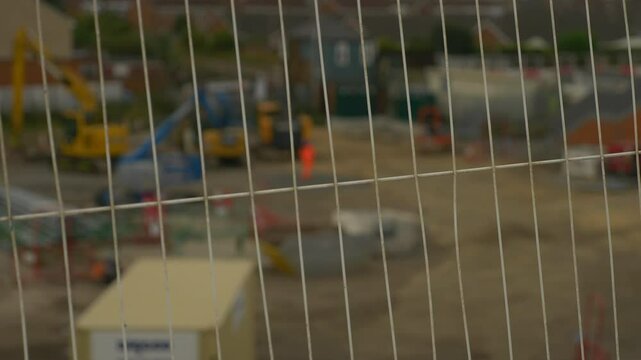 Construction Worker in Orange Work Clothes with Fence in foreground 