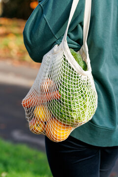 Woman Holding reusable Mesh grocery shopping Bag with Fresh Vegetables and fruits. Eco-friendly bag filled with fresh produce held by a person