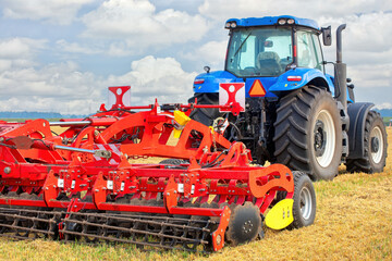 Vibrant blue tractor preparing farmland with red tillage equipment under a sunny sky