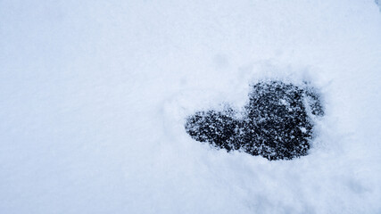 Heart shape love sign is drawn in snowy glade romantic background. Valentine's Day cold heart in snow winter season weather. Outdoor concept 