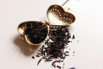 tea leaves inside of stainless steel tea bag and some of it scatter around with white background and soft light power