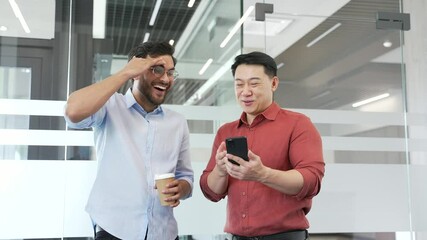 Two coworkers laughing and chatting over a phone in a modern business office. Happy cheerful team enjoying friendly conversation, fostering teamwork and workplace camaraderie during a casual moment