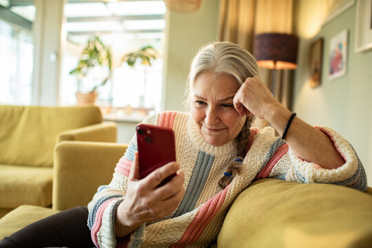 Smiling senior woman using smartphone on the couch at home