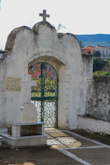 Ornate Stone Gate Structure with a Cross on Top: Concrete and Metal Gate with Intricate Ornaments on a Greek Island