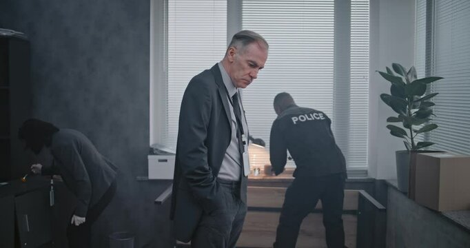 Office robbery or murder case: Crime investigation team working. Male detective in suit examines evidence at crime scene, female criminalist and African American policeman searches for fingerprints.