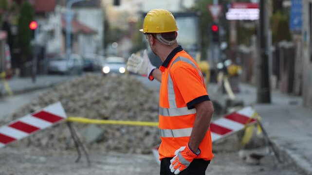 A nervous and stressed construction worker in a bright orange shirt manages traffic near an active road repair site, ensuring safety as vehicles navigate the area in the late afternoon.