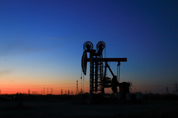 A silhouette of a pumping unit working in the evening