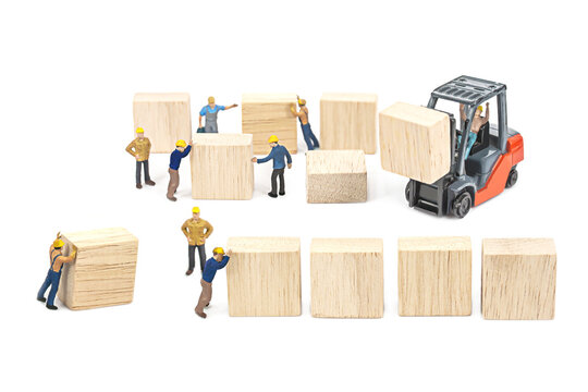 Selective focus of miniature worker people working front of forklift machine with wood block on white background.