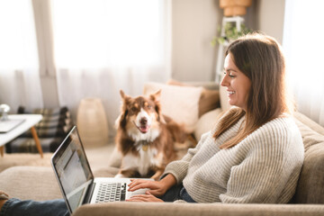 woman with cute fluffy Australian Shepherd dog at home using laptop computer in living room