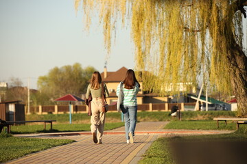 Two young girls dressed in fashionable clothes walk through a spring park in sunny weather. Girlfriends talking in nature. Walk in the fresh air.