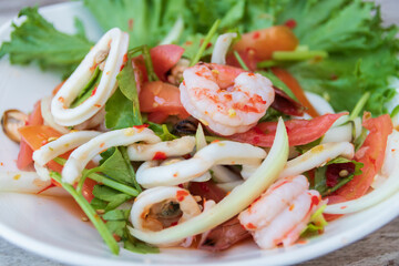 A vibrant seafood salad featuring fresh shrimp, squid, and vegetables, garnished with herbs on a rustic plate.