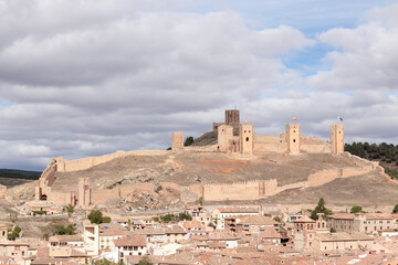 Majestic medieval castle with fortified walls overlooking a historic village under a cloudy sky