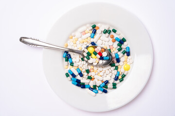 Metal spoon with A lot of Assorted pharmaceutical pills and colorful capsules on a white plate.