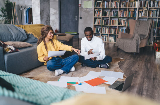 Smiling couple sitting on the floor, reviewing documents together in a cozy, home office setting. Surrounded by paperwork, they enjoy teamwork and communication, balancing work and personal life.