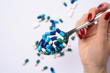 Female hand holding Metal spoon with A lot of Assorted pharmaceutical pills and colorful capsules. Capsules and medicine pills in background. Top view.