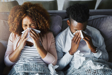Sick couple, sneeze and blowing nose with tissue on sofa for allergy, virus or flu and cold together above at home. Top view, young man and woman with influenza for sinus, symptoms or fever season