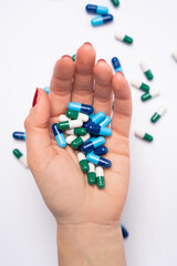 Female hand holding a lot of pharmaceutical pills and capsules, colorful medicine pills in blister packs in background.

