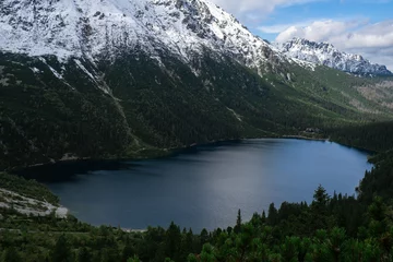 Morskie Oko Snowy Mountain Hut in Polish Tatry mountains, drone view, Zakopane, Poland. Aerial view shot of beautiful green hills and mountains in dark clouds and reflection on the lake Morskie Oko