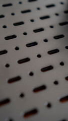A close-up of a perforated metal surface with a repeating pattern of oval and circular holes. The dark, industrial aesthetic creates a sense of mystery and intrigue.