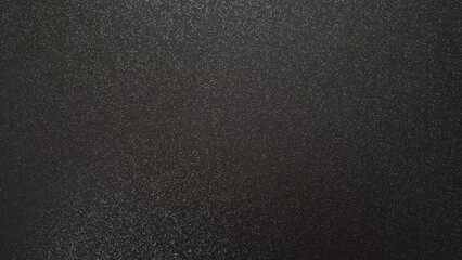 A close-up of a textured surface with a fine grain pattern. The dark, almost black color creates a...