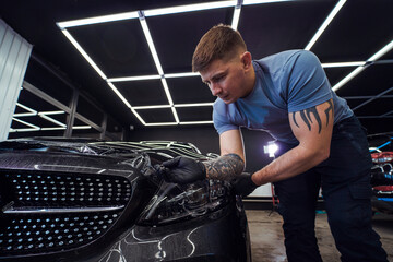 A tattooed man applies protective film to a black car