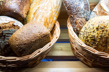 Various types of fresh bread in basket on shelf in bakery.