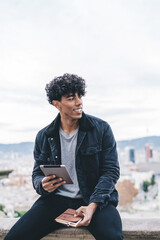 Joyful ethnic man browsing tablet on street