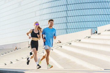 Fototapeta premium A Young Couple Jogging Together on Outdoor Steps in a Modern Urban Setting During Sunny Weather