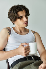 A young man with tattoos enjoys a moment of contemplation while holding a cup of coffee.