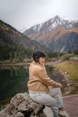 Fototapeta premium Happy travel girl sitting on rock by the mountain lake and looking at view in autumn at Dagu Glacier Park , China.People with landscape concept.