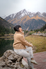 Happy travel girl sitting by the mountain lake and looking at  view in autumn at Dagu Glacier Park , China.People with landscape concept.