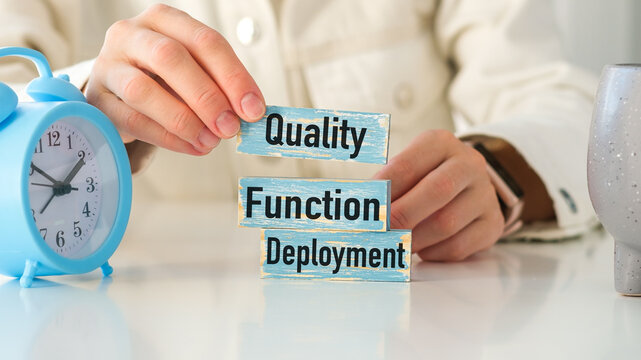 A person holding up a blue clock and a stack of wooden blocks with the words Quality Function Deployment written on them