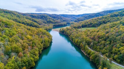 Obraz premium Aerial view of a serene river winding through lush green hills under a partly cloudy sky.