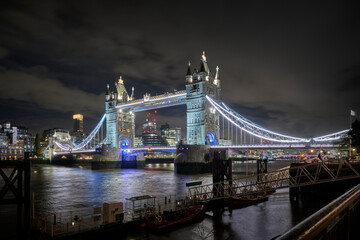 The illuminated Tower Bridge stands majestically at night, surrounded by a lively urban atmosphere.