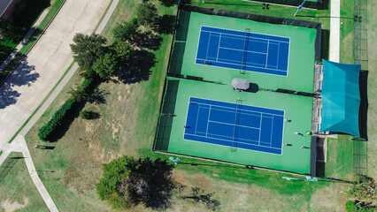 Close-up modern lighted tennis court in sport complex outside Dallas Texas, well-lit hard courts with player practicing group lesson, shaded spectator areas and comfortable benches, ball machine