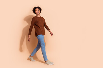Fototapeta premium Cheerful young African American man walking confidently in casual outfit against a beige background