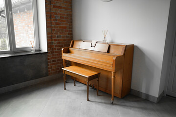 A classic wooden piano and matching bench placed against a brick wall in a modern interior setting...